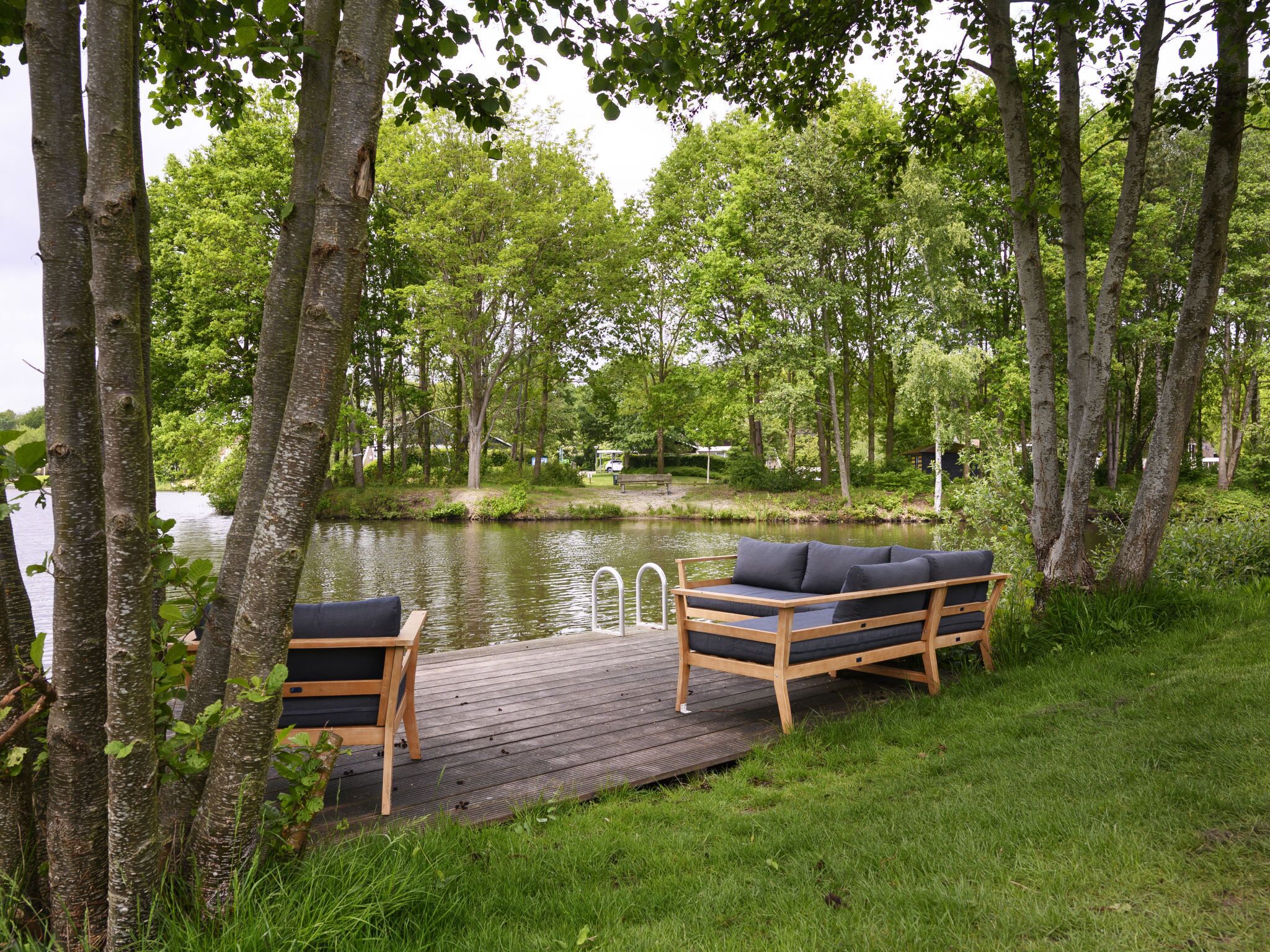 A wooden deck with a sofa and chair by a lake, surrounded by trees.