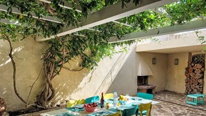 Une terrasse extérieure avec un sol en pierre, une table dressée pour le repas et une cheminée en pierre.