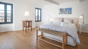 Une chambre à coucher avec un grand lit, deux tables de chevet avec des lampes, un banc et un tableau au mur.