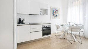 A modern kitchen with white cabinetry, a built-in oven, and a dining area with a glass table and white chairs.