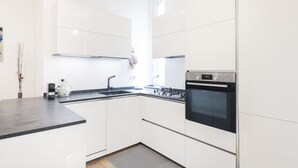 A modern kitchen with white cabinets, a black countertop, a built-in oven, and a coffee maker.