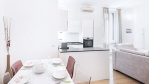 A modern, well-lit kitchen with white cabinetry, a central island, and a dining area with a white table set for four.