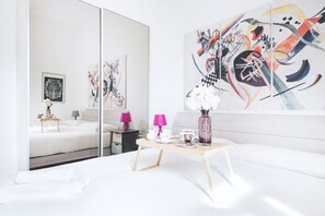A modern hotel room with a large mirror, a bed, a small table with tea set, and abstract art on the wall.