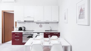 Une cuisine moderne avec des meubles blancs, une table à manger pour quatre personnes et une porte à cadre rouge.
