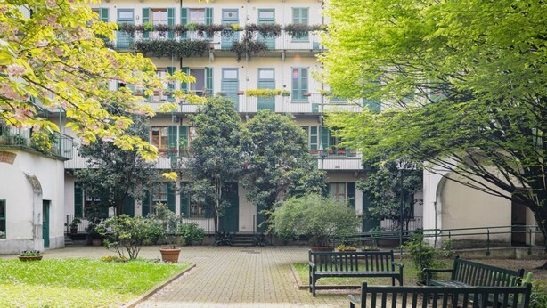 Une cour avec un chemin pavé, des bancs et une végétation luxuriante.
