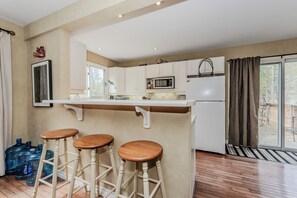 Una cocina con armarios blancos, un microondas, un refrigerador y una zona con taburete de bar.
