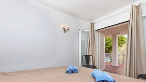 A room with a bed, two rolled towels, a chair, and a view of an outdoor balcony.