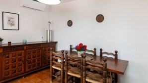 A dining area with a wooden table and chairs, a hanging light fixture, a cabinet with multiple doors, and a wall-mounted air conditioner.