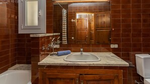 A bathroom with a marble sink, wooden cabinets, a bathtub, and a mirror with a light above it.