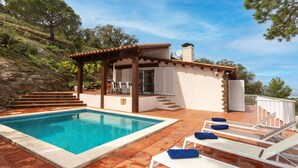 Zona de piscina con piscina, sillones de descanso y un pequeño edificio con pérgola.
