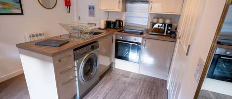 Une cuisine compacte équipée d’un lave-linge, d’un four, d’un four à micro-ondes et d’une machine à café.