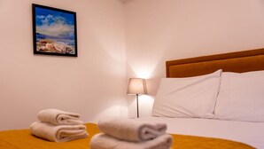 A hotel room with a neatly made bed, a lamp, and a painting on the wall.