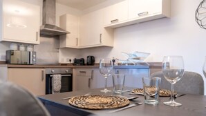 A modern kitchen with white cabinets, a microwave, and a coffee maker. There are four wine glasses and a small table with placemats.