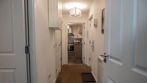 A narrow hallway with white walls, a carpeted floor, and a door on the right.