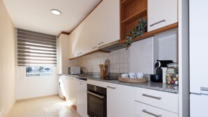 Una cocina moderna con armarios blancos, horno empotrado y encimera con diversos electrodomésticos y utensilios.