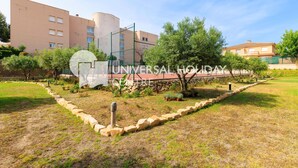 Un patio con cancha de tenis, un sendero de piedra y un edificio de fachada color crema.