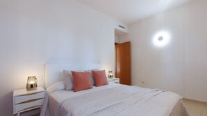 Un dormitorio con cama, dos mesitas de noche, una lámpara de noche y una puerta.
