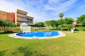 A swimming pool surrounded by grass, with a building in the background. - 164 UHC TRAMUNTANA APARTMENTS (Salou)