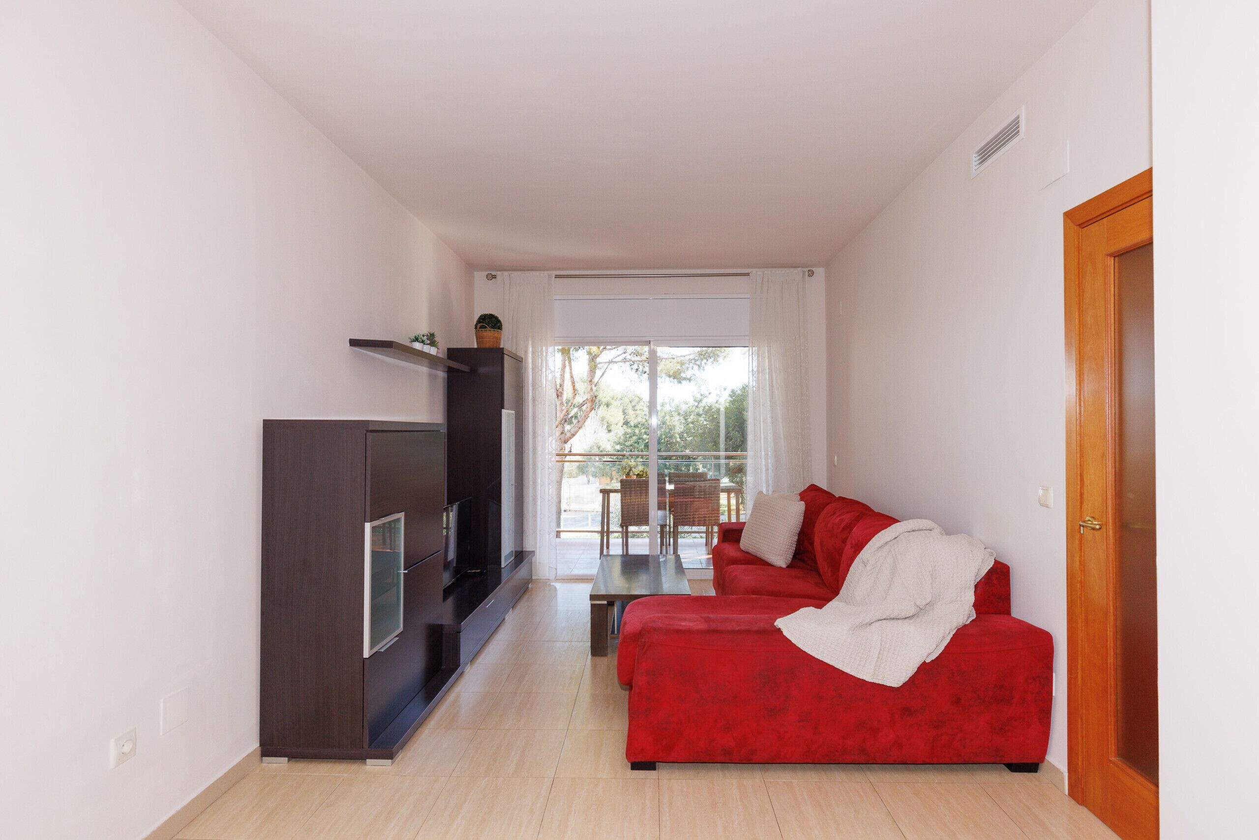 Ein modernes Wohnzimmer mit einem roten Sofa, einem Flachbildfernseher und einer Glastür, die auf einen Balkon führt.