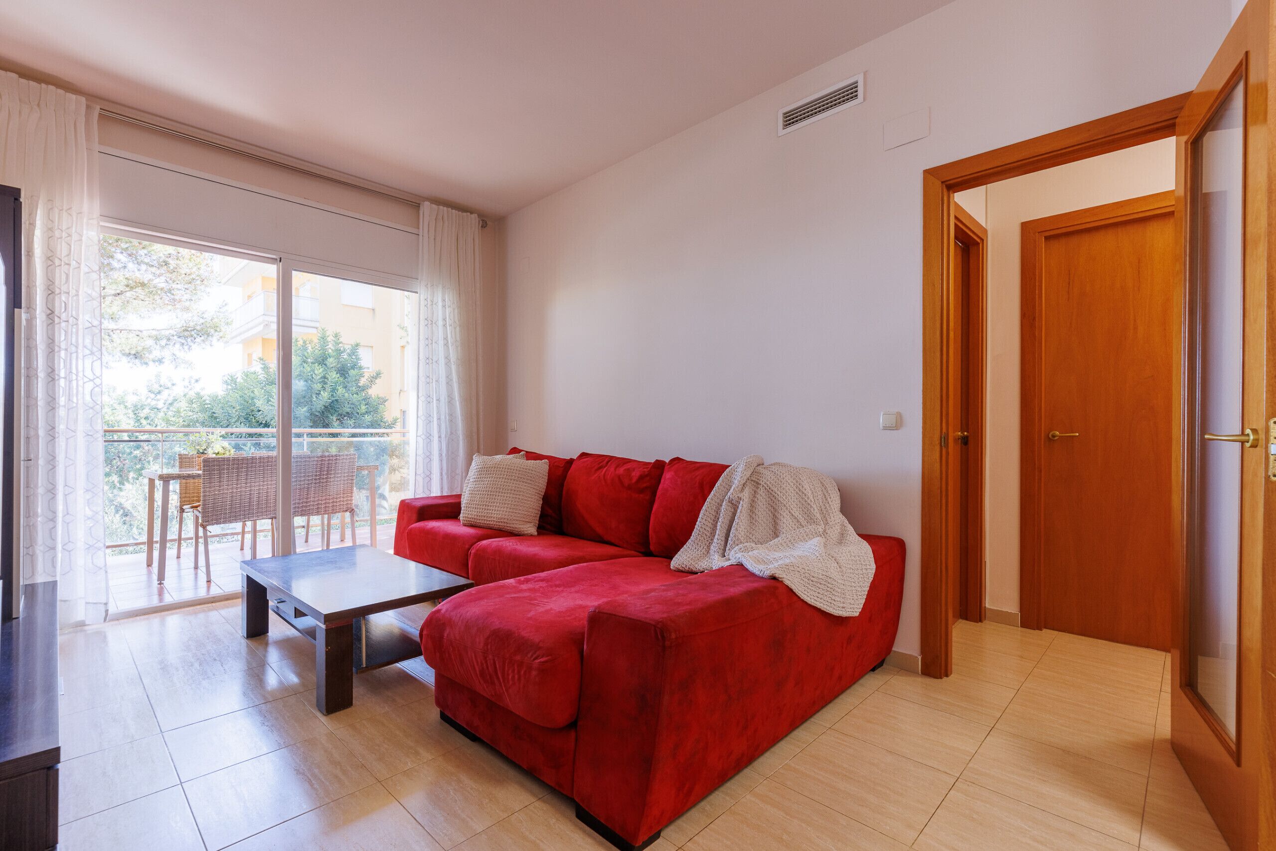 A red sofa, a wooden table, and a balcony with wicker chairs.