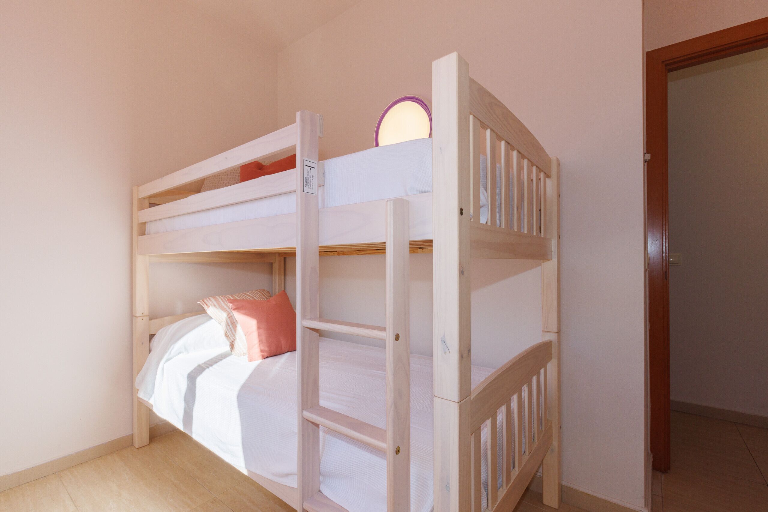 A bunk bed with a ladder, a small mirror, and a door to another room.