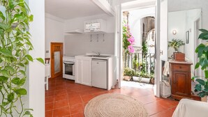 A spacious kitchen with white cabinets and a built-in oven, a dining area with a round rug, and a balcony with potted plants and flowers. - Casa Livia Sperlongaresort (Sperlonga)