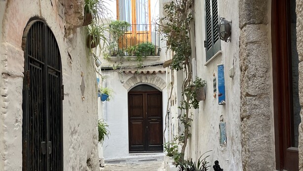 A narrow stone-paved alleyway with a central door and arched windows, flanked by buildings with white walls and black doors. - Casa Livia Sperlongaresort (Sperlonga)