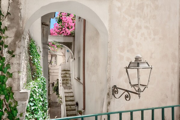 A narrow stairway leading to a door, a wall-mounted lantern, and a stone wall with greenery.