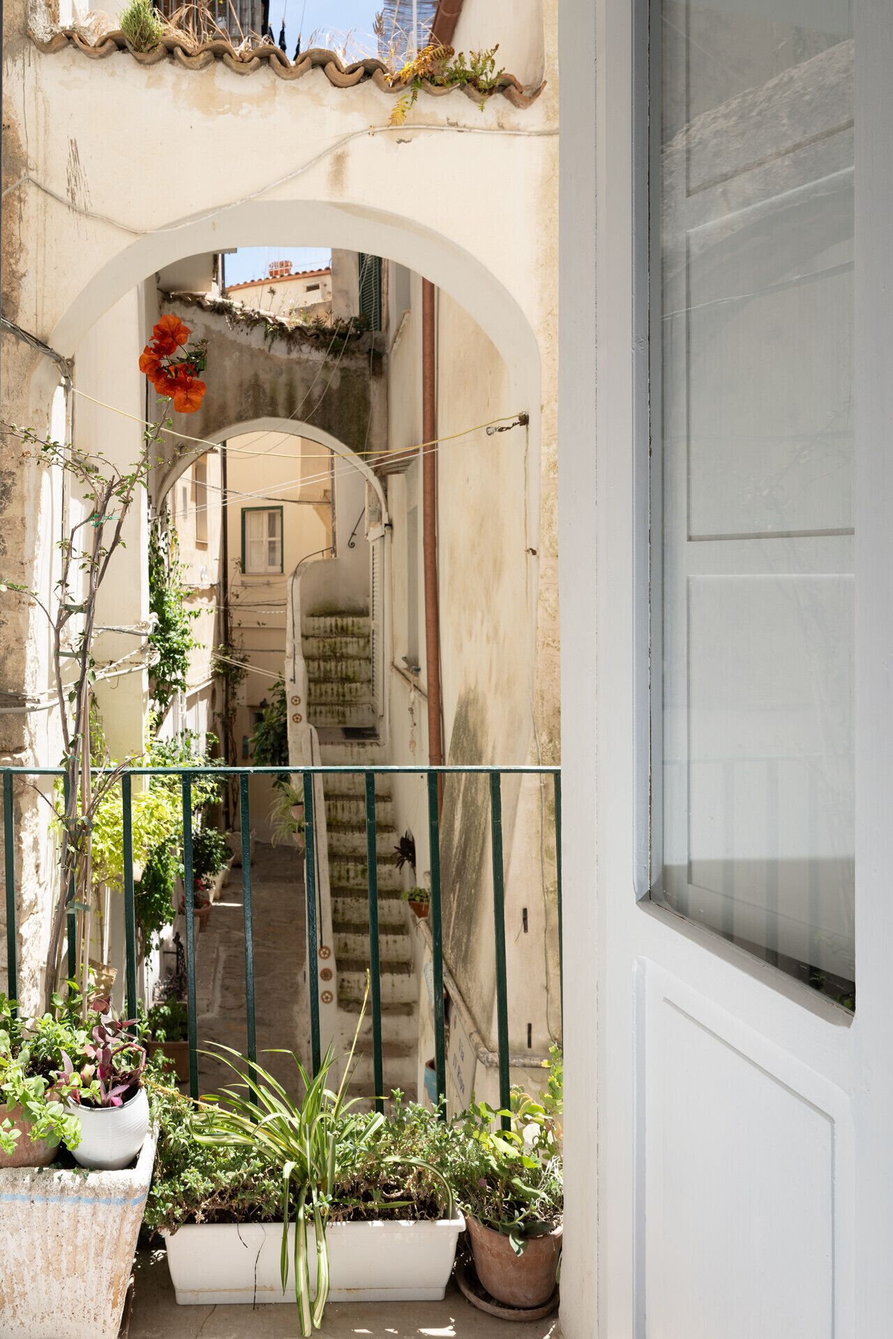 Ein Balkon mit Außenbereich und Blick auf eine enge Straße, eine Treppe und eine Tür.