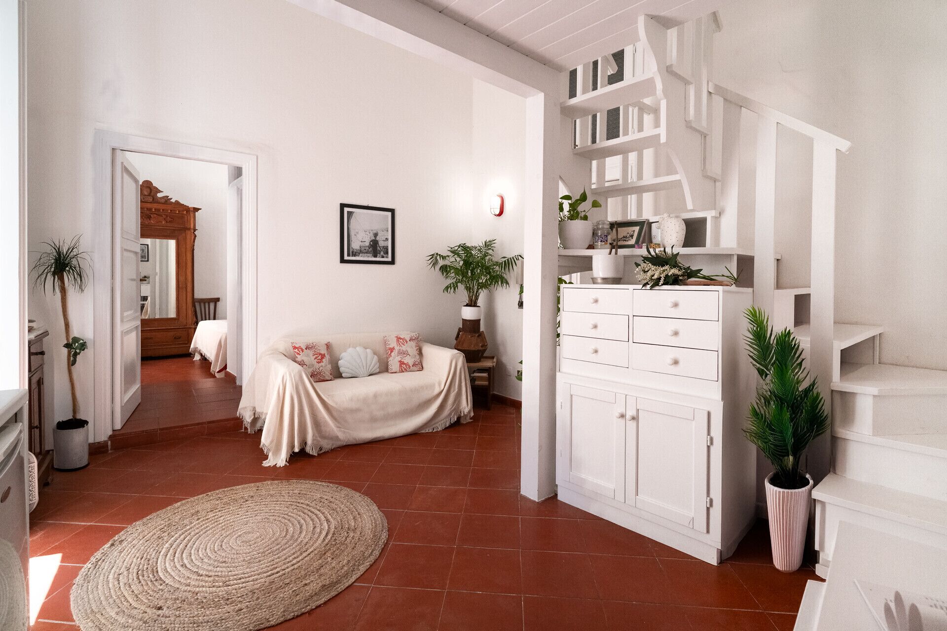 A spacious living area with a sofa, a large woven rug, and a white cabinet with shelves.
