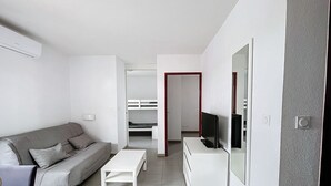Una sala de estar moderna y minimalista con un sofá gris, una mesa de centro blanca y un televisor sobre un mueble blanco.