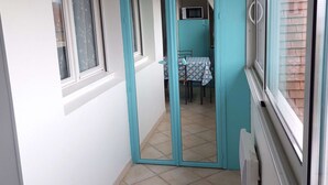 En smal gang med teal-malede vægge og hvide detaljer, der fører til et spiseområde med bord og stole.