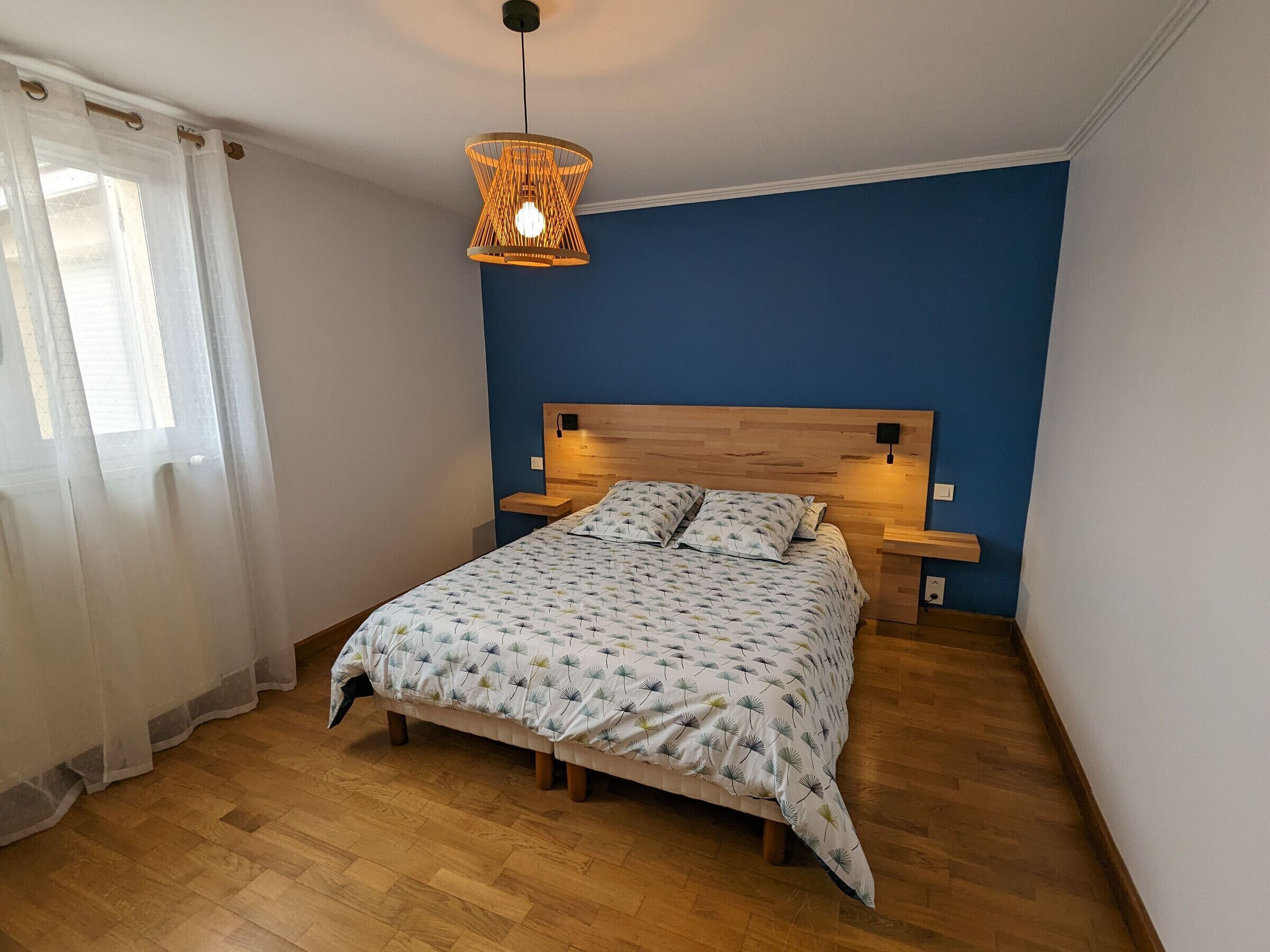 Una camera da letto con un letto di legno, una parete azzurra, un lampadario e un comodino con una lampada.