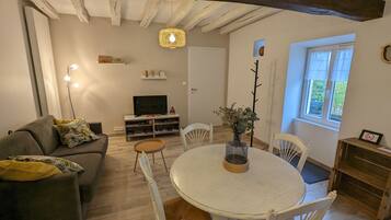 Een gezellige woonkamer met een bank, een ronde eettafel en een televisie.