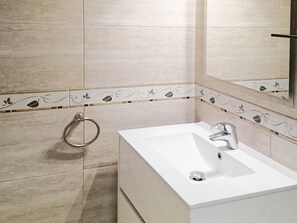 A bathroom with a white sink, a mirror, and decorative tiles with leaf patterns. - Cozy 5-Person Apartment with Pool, 800m to Beach and City Center (L'Estartit)