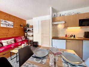 Un salon chaleureux avec un canapé rouge, une table à manger dressée avec des assiettes et des verres, et un coin cuisine équipé d’un four à micro-ondes et de placards.