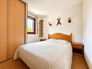 A bedroom with a wooden bed, a nightstand, a shelf, and a window with curtains.