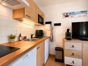 Eine kompakte Küche mit Geschirrspüler, Kaffeemaschine, Fernseher und einem kleinen Mülleimer.