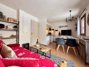 Un espace de vie compact comprenant un canapé, une table à manger, des chaises, un coin cuisine et un téléviseur.