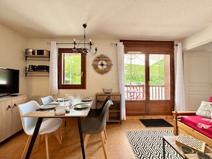 A dining area with a table set for four, a television, and a clock on the wall.