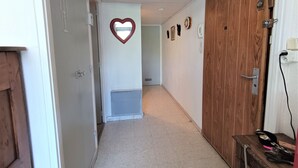 A hallway with a wooden door, a heart-shaped decoration on the wall, and a small table with items on it.