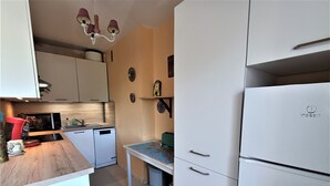 A compact kitchen with white cabinets, a microwave, a coffee machine, and a refrigerator.