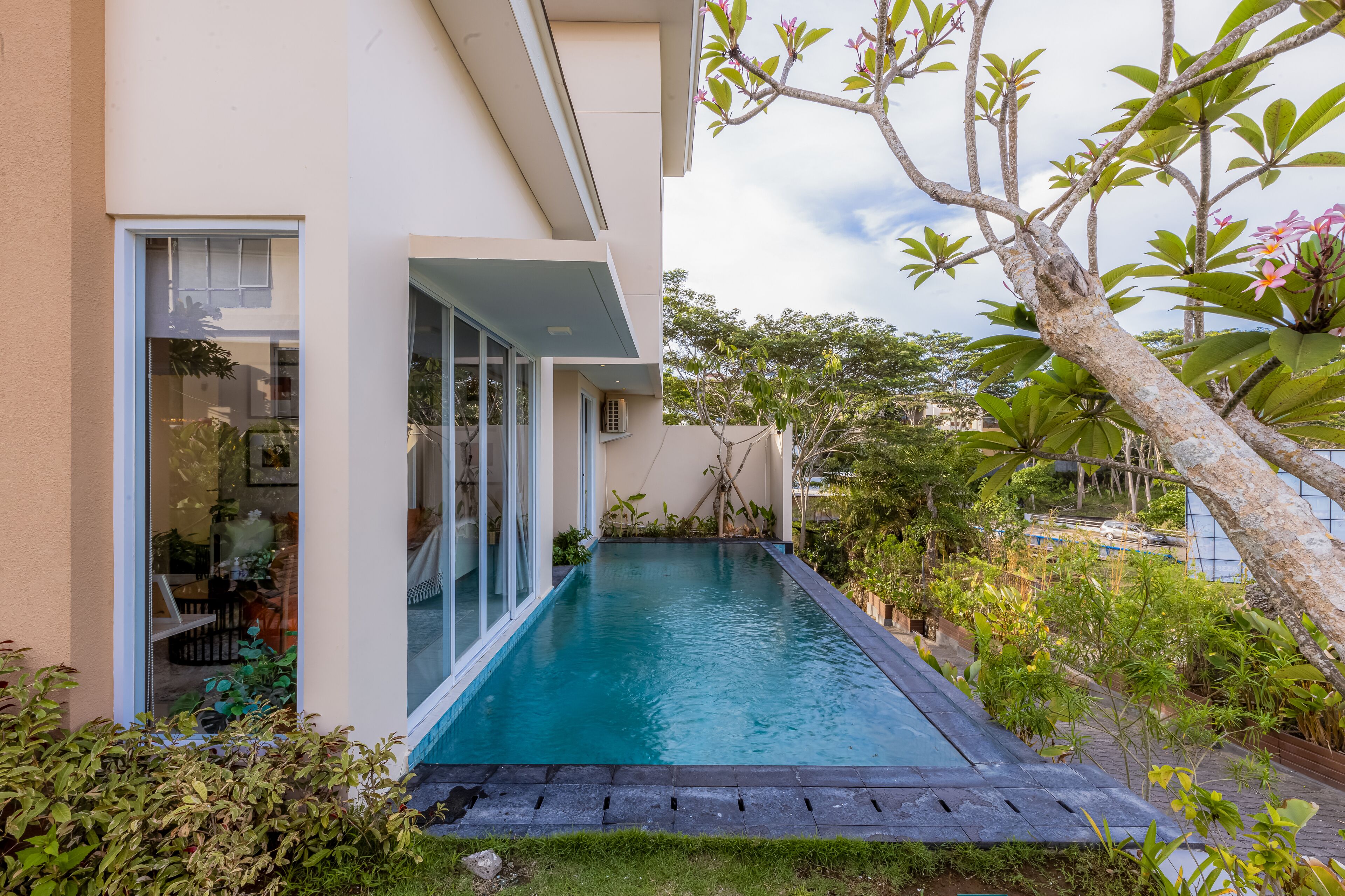 A modern house with a swimming pool, large glass doors, and lush greenery.