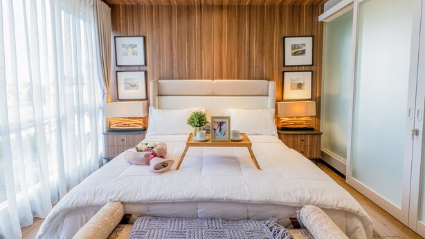 Un dormitorio moderno con techo de madera, una cama grande con ropa de cama blanca, lámparas de noche y cuadros en las paredes.