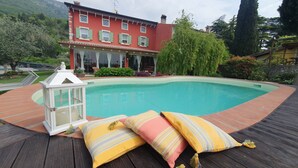 Una piscina con cubierta de madera, rodeada de exuberante follaje y un edificio rojo con varias ventanas.