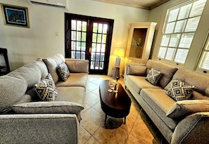 A living room with two sofas, a coffee table, and a lamp. There is a door with glass panels and a framed picture on the wall.