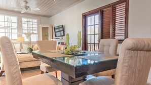 Un comedor con una mesa de vidrio, sillas acolchadas y una televisión al fondo.