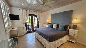 Un dormitorio con una cama grande, un ventilador de techo, un televisor, una ventana con cortinas y una puerta que da al exterior.
