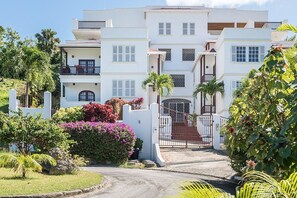Un hotel de varios pisos con fachada blanca, balcones y entrada protegida por una reja.