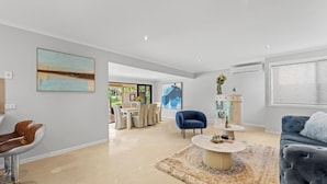 A modern living room with a large window, a dining area, and a blue armchair. - Serene Lakefront Water side Villa with Private Pool  (Westlake)